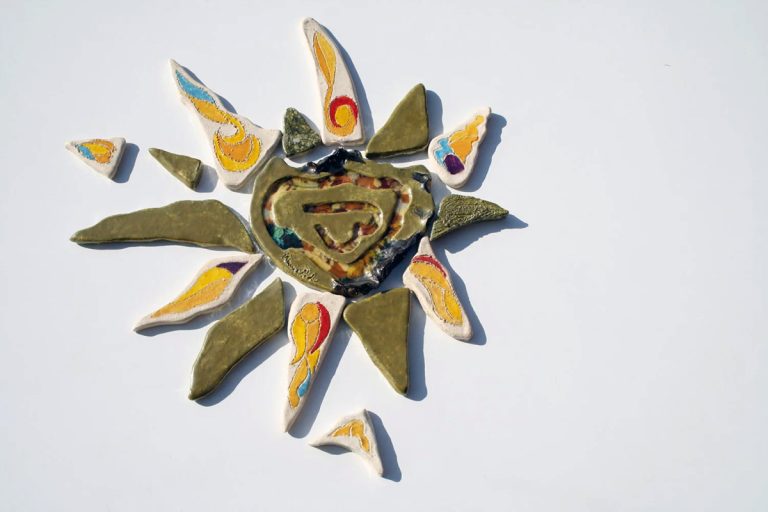 Scultura ceramica in argilla bianca con fulcro a effetto lustro iridescente, vetri fusi e raggi multicolore in giallo, azzurro, rosso e argento