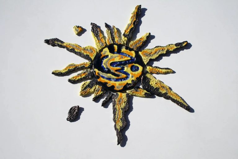 Scultura ceramica di medio formato con fulcro e raggi in refrattario bianco, caratterizzata da graffi istintivi, tessere di vetro fuso e smalti nero metallico, arancio e giallo