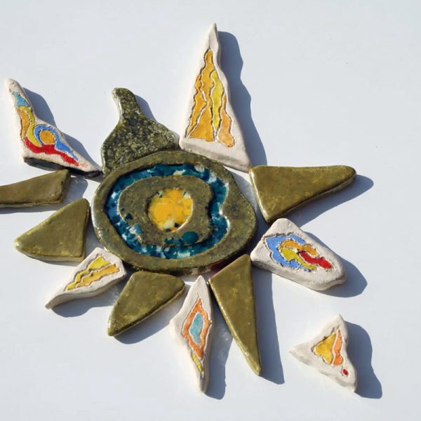 Scultura ceramica di piccolo formato con nucleo centrale iridescente a base lustro, inserti in vetro fuso e raggi nei toni del giallo, rosso, blu e argento