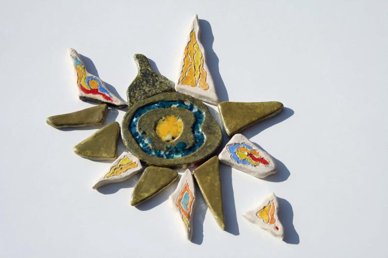 Scultura ceramica di piccolo formato con nucleo centrale iridescente a base lustro, inserti in vetro fuso e raggi nei toni del giallo, rosso, blu e argento
