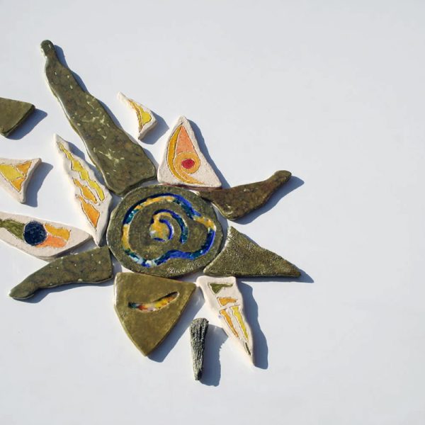 Scultura ceramica di medio formato in argilla bianca con fulcro iridescente, vetri fusi e raggi radiali colorati in giallo, azzurro e argento