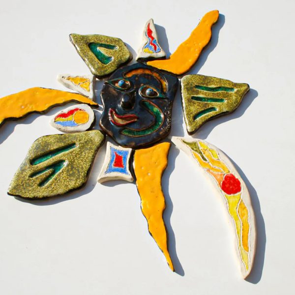 Scultura ceramica con fulcro in argilla rossa a forma di maschera nera sorridente, inserti in vetro fuso e raggi multicolore con finitura lustro