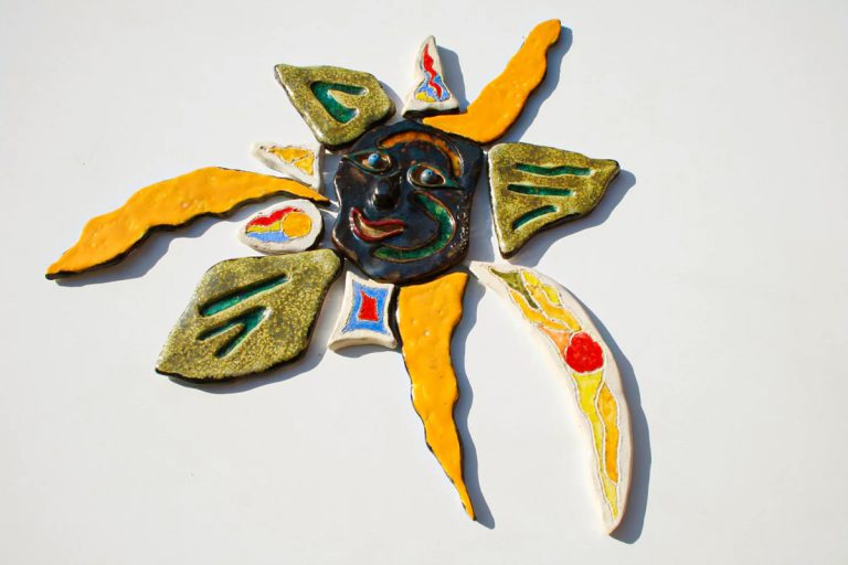 Scultura ceramica con fulcro in argilla rossa a forma di maschera nera sorridente, inserti in vetro fuso e raggi multicolore con finitura lustro