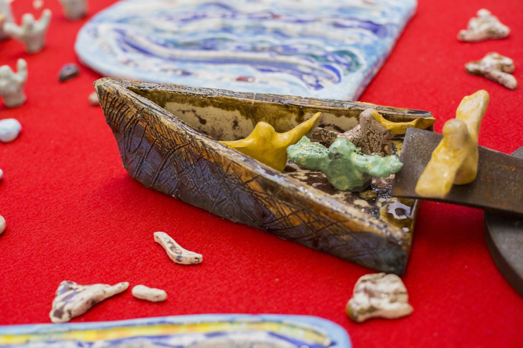 Scultura ceramica di barca simbolica con figure umane, rappresentazione di speranza, migrazione e ricerca di un approdo