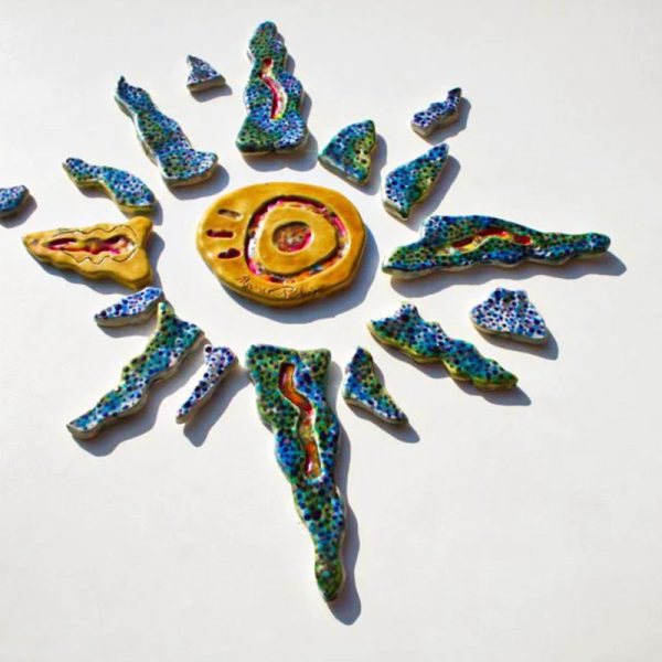 Scultura ceramica di medio formato con raggi decorati in blu e verde, fulcro ocra con elementi grafici e inserti in vetro fuso