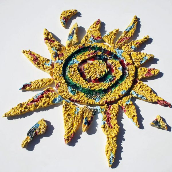 Scultura murale in argilla bianca con elementi separati, sfera centrale gialla con vetri fusi e raggi con graffi materici in rosso e azzurro