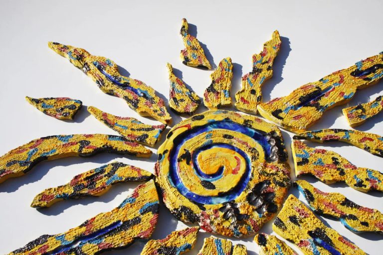 Grande scultura murale in refrattario bianco con fulcro e raggi incisi, smalti oro e arancio e inserti in vetro fuso