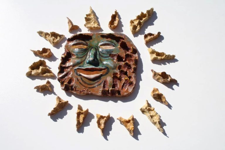 Piccola scultura di sole in ceramica con raggi graffiati e incisi e una maschera centrale dall'espressione ironica e divertente.