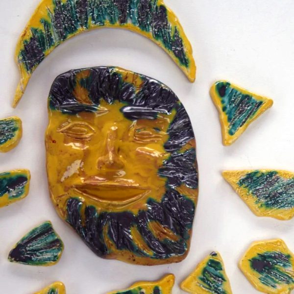 Sole in refrattario bianco con volto sorridente, raggi graffiati e finiture cangianti in smalto argento e giallo.
