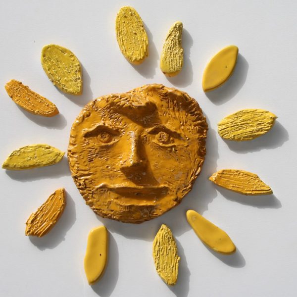 Sole scultoreo con nucleo centrale giallo-arancio dalle sembianze umane e raggi disposti in modo asimmetrico.