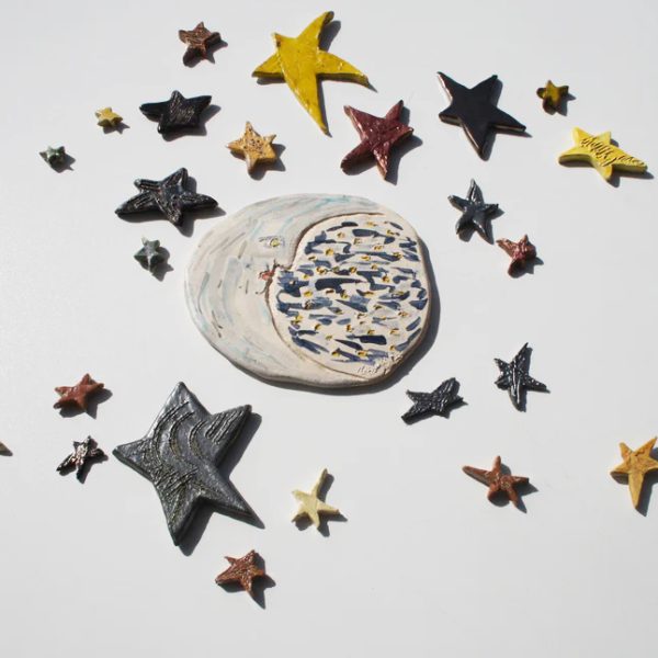 Luna scultorea media in ceramica bianca con sfumature argento e azzurre, circondata da stelle di varie dimensioni.