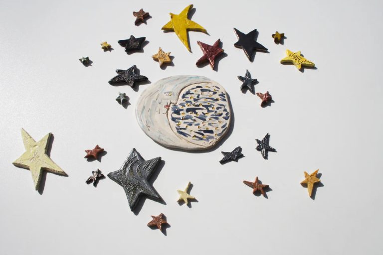 Luna scultorea media in ceramica bianca con sfumature argento e azzurre, circondata da stelle di varie dimensioni.