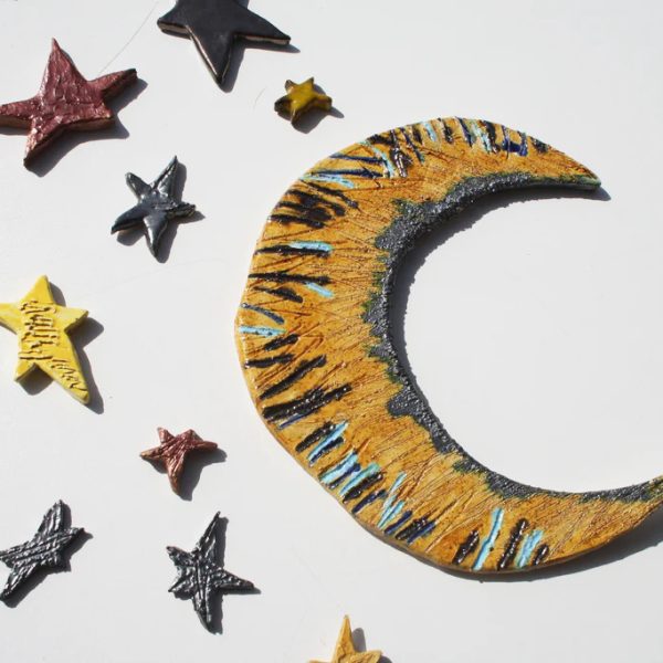 Luna in ceramica posizionabile in modo crescente o decrescente, rifinita con smalti vivaci e stelle multicolore.