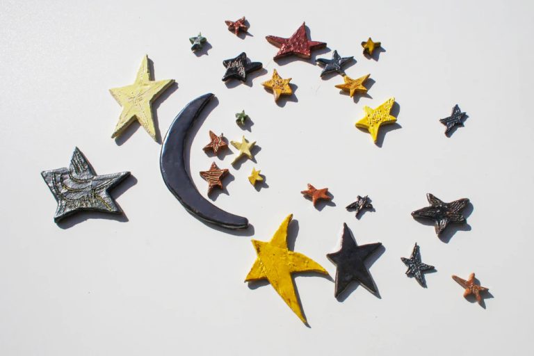 Piccola scultura di luna in ceramica bianca con smalto speciale cangiante e un seguito di stelle artigianali.