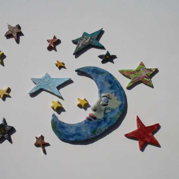 Grande luna crescente celeste in ceramica con espressione ironicamente seccata, affiancata da stelle.