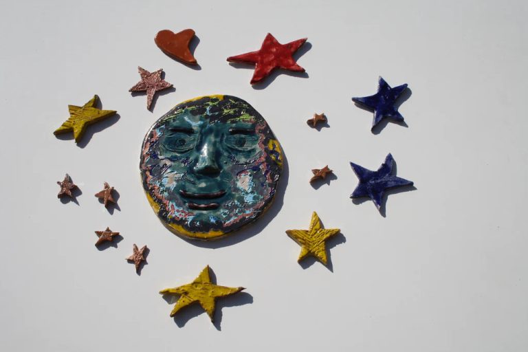 Semiluna in ceramica bianca con volto sorridente e finitura smaltata scintillante, circondata da stelle colorate.