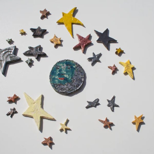 Luna in ceramica smaltata in blu intenso con volto dall'espressione attenta e un contorno dinamico di stelle assortite.