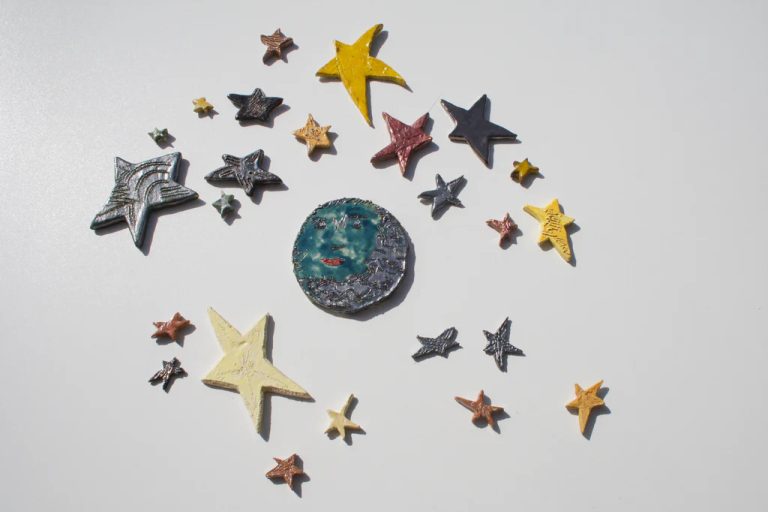 Luna in ceramica smaltata in blu intenso con volto dall'espressione attenta e un contorno dinamico di stelle assortite.