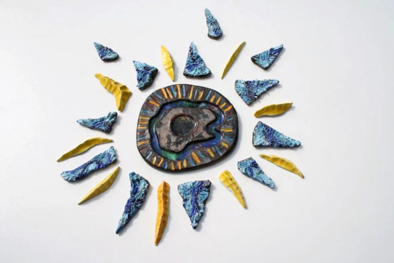Sole in ceramica medio-piccolo con fulcro centrale color bronzo e vetro fuso, raggi gialli a fiammella e raggi blu incisi.