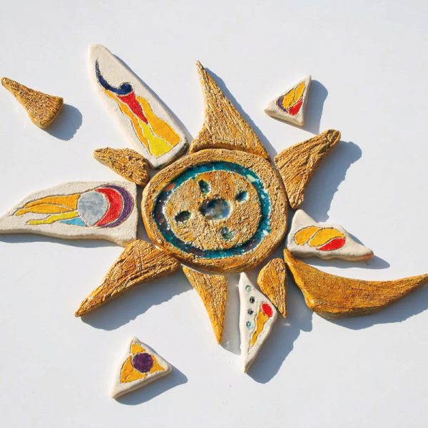 Piccolo sole raffinato in argilla bianca con nucleo cangiante color miele e vetro fuso, circondato da una raggiera multicolore brillante.