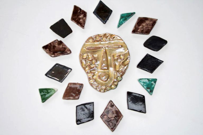 Piccolo sole scultoreo in ceramica dall'espressione extraterrestre rossa con raggi asimmetrici bianchi smaltati in marrone Dorré, nero e oro metallico.