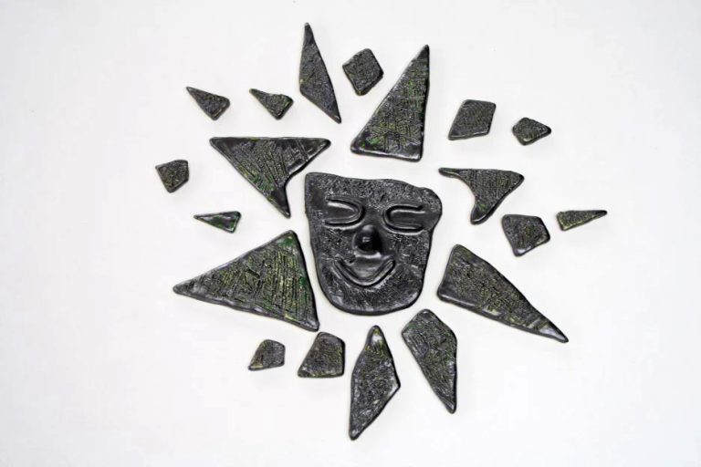 Sole di formato medio interamente rivestito di smalto argento riflettente, con fulcro graffiato e volto amichevole al centro.