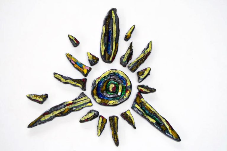 Piccolo sole in creta nera con graffiti manuali, sfumature gialle e arancioni e un nucleo centrale con inserti di vetro fuso.