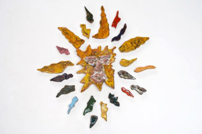 Sole medio in argilla rossa con volto felice bianco-giallo e una raggiera multicolore arricchita da cristallina scintillante e lustri metallici.