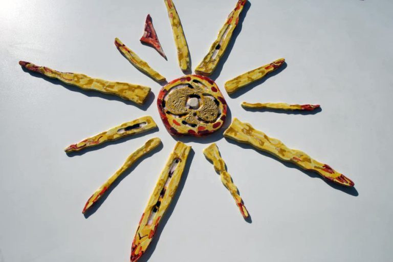 Grande sole in ceramica con pennellate gestuali di gialli, solchi centrali con tessere di vetro fuso e raggi in espansione.