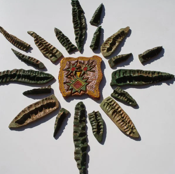 Grande sole scultoreo dalle linee asimmetriche e irregolari, smaltato con dettagli espressivi e ironici.